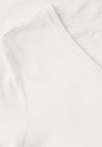 Bílý V-krkový tričko vyrobené z měkké, lehké tkaniny. Má ploché švy a hladkou texturu, s čistým, minimalistickým designem.