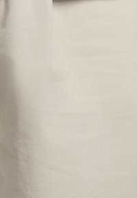 Μπεζ ύφασμα με διακριτική υφή και μια απαλή σκιά στην αριστερή πλευρά.