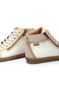 Zapatillas altas de cuero crema y gamuza beige. Presentan cremallera y ojales en tono bronce, suela de goma texturizada y detalles de costura.