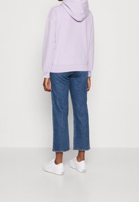 Felpa viola con cappuccio, vestibilità ampia, polsini a costine, abbinata a jeans blu scuro a gamba larga e sneakers bianche. Tessuto testurizzato, stile casual.