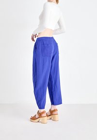 Pantalon bleu ample en tissu côtelé avec une taille élastique et deux poches arrière, porté avec des sandales marron à talons.