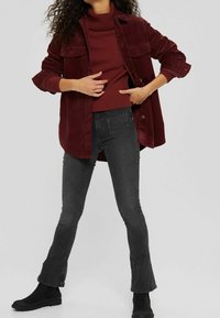 Chemise en velours côtelé bordeaux superposée à un col roulé bordeaux côtelé, associée à un jean noir évasé et des bottines noires.