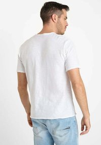 Witte T-shirt met korte mouwen en ronde hals, gemaakt van een gestructureerde stof, gecombineerd met lichtblauwe jeans. De pasvorm is casual en ontspannen.