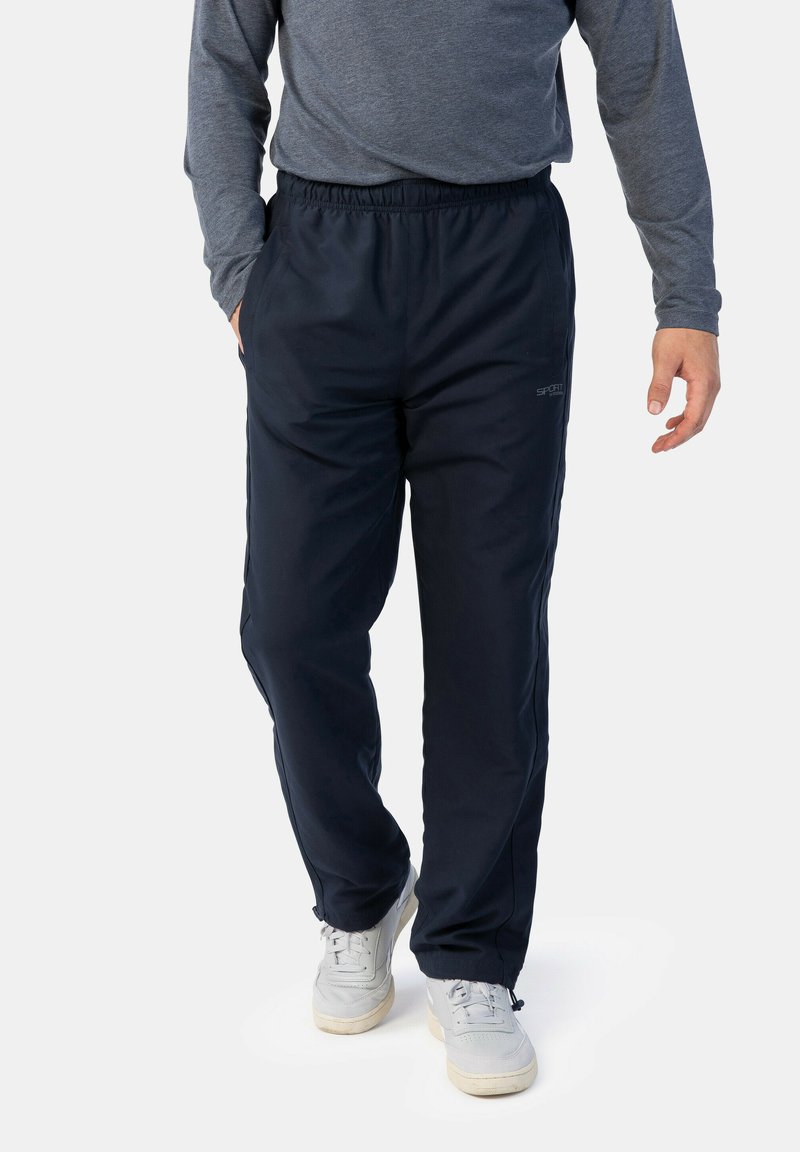 Marinefarbene Sporthosen aus einem glatten Stoff mit einem elastischen Bund, ausgestattet mit Seitentaschen und Reißverschlüssen an den Knöcheln zur Anpassung.