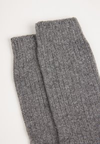 Calcetines de lana gris con una textura acanalada, que transmiten una apariencia suave y cálida. Los puños son gruesos y elásticos, diseñados para mayor comodidad.