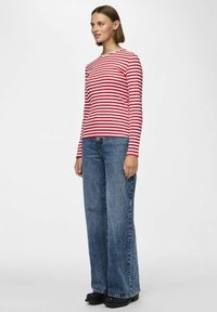 Röd och vitrandig långärmad tröja i kombination med högmidjade vida blå jeans. Tröjan har en rund halsringning och en figurnära design.