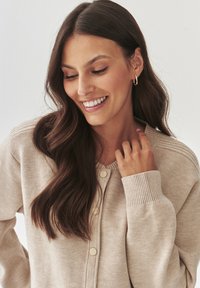 Licht beige cardigan gemaakt van zachte stof, met ribgebreide manchetten, een knoopsluiting aan de voorkant en een minimalistisch ontwerp zonder patronen of versieringen.