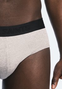 Brief en coton gris avec une ceinture élastique noire portant le logo "ALLSAINTS". Texture lisse et design ajusté avec des détails cousus.