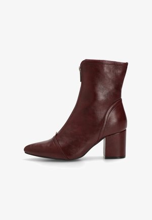 Botín de piel burdeos hasta el tobillo con punta afilada y tacón cuadrado. Presenta un cierre lateral con cremallera y una textura suave, con detalles de costura.