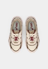 Μπεζ και καφέ αθλητικά παπούτσια με υλικά από δικτυωτό και δέρμα, διαθέτοντας στρογγυλή μύτη, κορδόνια και κόκκινο λογότυπο στην εσωτερική σόλα.