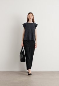 Top senza maniche nero con una texture liscia, abbinato a pantaloni neri su misura e una borsa a tracolla nera strutturata. Sfondo neutro.