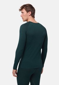 Camicetta fitted verde a maniche lunghe realizzata in materiale morbido, con scollatura rotonda e cuciture piatte, mostrata da un'angolazione laterale.