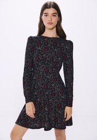 Svart blommig klänning med långa ärmar, med ett röd- och grönt blommönster, rundad halsringning och en figurnära midja som svänger ut vid midjan.