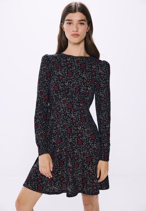 Zwarte bloemenjurk met lange mouwen, voorzien van een rood en groen bloemenpatroon, een ronde halslijn en een getailleerde pasvorm die uitloopt bij de taille.