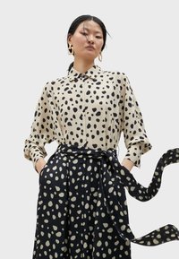 Camicia beige con bottoni a Pois neri abbinata a una lunga gonna nera con motivo a Pois simili e una cintura annodata in vita.