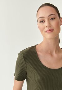 Oliivroheline ribiga T-särk lühikeste varrukatega ja ümar kaelus. Kangas näeb välja pehme, sileda tekstuuriga ja peente vertikaalsete joontega.