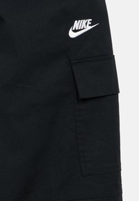 Čierne nákladné šortky z textúrovaného materiálu s prekrytým vreckom a bielym logom Nike. Dizajn obsahuje mriežkový vzor.