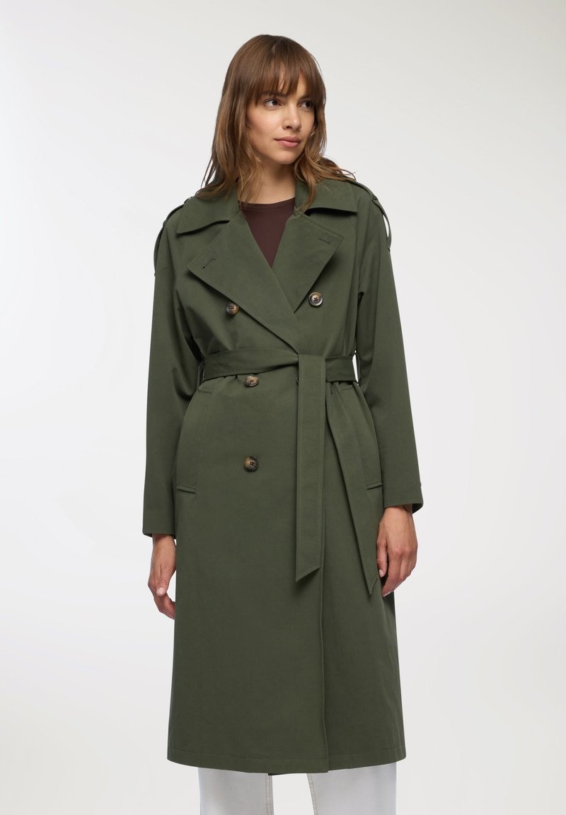 Oliwkowy płaszcz trench z podwójnym zapięciem, dużymi guzikami i wiązaniem w talii. Posiada epoletki oraz długie rękawy o dopasowanym kroju.
