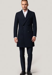 Czarny, granatowy płaszcz dwurzędowy z klapami, dopasowany krój, kieszeniami bocznymi i wyrazistą sylwetką, noszony na dopasowanych spodniach.
