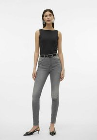 Top negro sin mangas, jeans ajustados gris de cintura alta, cinturón negro y tacones negros tipo slingback. Textura suave y diseño ajustado.