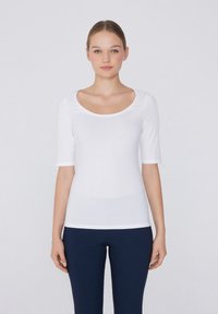 Top bianco a maniche corte con scollo tondo, realizzato in tessuto liscio. Design aderente, abbinato a pantaloni blu scuro. Stile minimalista.