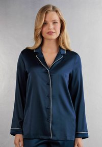 Navy satin pyjamas topp med långa ärmar, en notch-krage, vit pipning och knäppning fram. Slät textur och avslappnad passform.