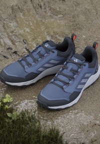 Chaussures de trail bleues et noires avec semelles blanches, placées sur de la terre humide et de l'herbe en extérieur.