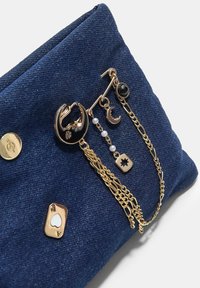 Pochette en denim bleu foncé avec des accents de chaîne et de charme en or. Présente des motifs ronds et étoilés, ainsi qu'un détail de carte à jouer.