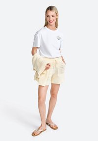 Witte katoenen t-shirt met een tennisracket graphic, gecombineerd met lichtgele gebreide shorts met een trekkoord. Sandalen maken de outfit compleet.