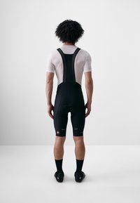Shorts de cyclisme noirs avec bretelles en mesh, dotés d'un rembourrage au niveau de l'assise et d'accents réfléchissants. Portés avec un sous-vêtement à manches courtes blanc.