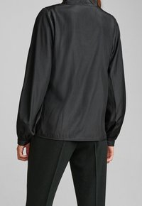 Chemise noire à manches longues avec une texture lisse et brillante, dotée d'une coupe décontractée, de poignets élastiques et d'un col classique.