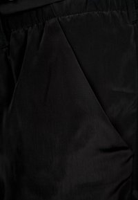 Svart tyg som visar en slät, matt textur med en subtil lyster. Har en noggrant sydd ficka med rundade kanter.