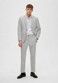 Traje ajustado en gris claro con chaqueta entallada y pantalones slim, combinado con una camisa de vestir a rayas blanca y azul y zapatos negros.
