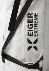 Bílý tkaný batoh s diamantovým vzorem, s černými popruhy a brandy "EIGER EXTREME" a "MAMMUT." Viditelné detaily texturovaného povrchu.