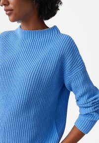 Maglione azzurro chiaro lavorato a maglia con una texture a coste, scollo a barca e maniche leggermente a sbuffo. Senza motivi visibili o dettagli in metallo.