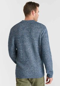 Stickad tröja i ett blått melange-mönster med ribbad krage och mudd. Har en avslappnad passform och texturerad yta.