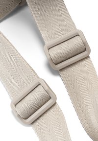 Două bretele din țesătură bej, cu catarame dreptunghiulare din plastic pentru ajustare, pe un fundal alb.