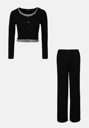 Schwarzes Loungewear-Set bestehend aus einem gekürzten Langarmoberteil mit grauem Saum und Knopfverschluss, kombiniert mit locker sitzenden schwarzen Hosen.