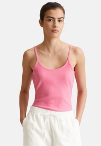 Pink ribbelndes Tanktop mit dünnen Trägern, das einen runden Halsausschnitt und ein figurbetontes Design aufweist. Kombiniert mit weißen Jogginghosen mit Kordelzug.