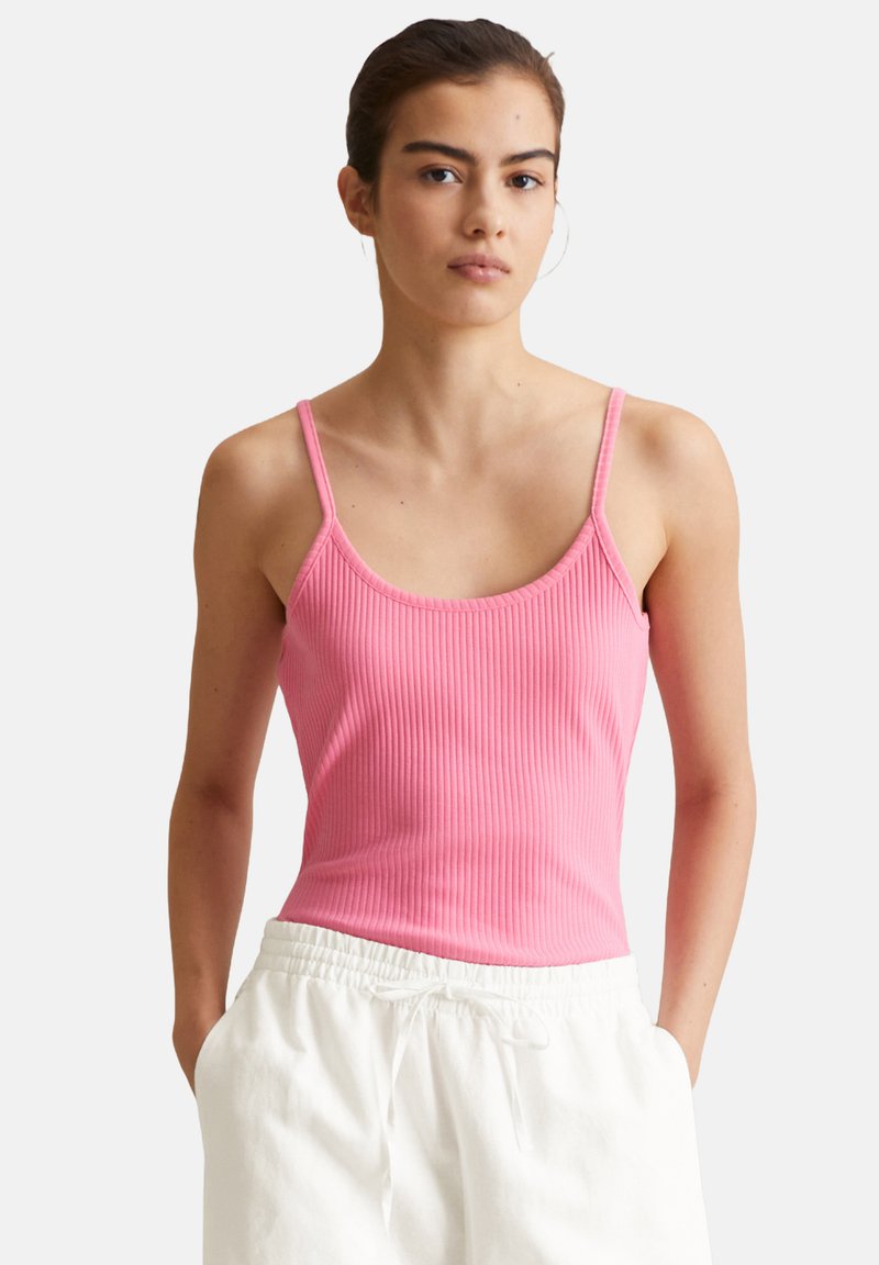 Pink ribbelndes Tanktop mit dünnen Trägern, das einen runden Halsausschnitt und ein figurbetontes Design aufweist. Kombiniert mit weißen Jogginghosen mit Kordelzug.