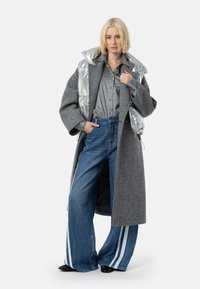 Pilkos vilnos paltas per sidabrinį pūkų liemenę, derinamas su plačiomis džinsinėmis kelnėmis, turinčiomis baltas šonus ir juodais batais.