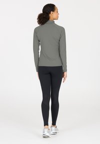 Langærmet, grå træningstrøje med ståkrave, parret med sorte leggings med teksturerede udskæringer og reflekterende detaljer.