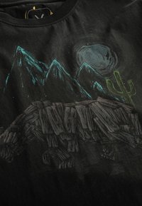 Zwarte T-shirt met een graphic design van bergen, een maan en een cactus. Bevat structuren die houtachtig lijken voor de silhouet van de beer.