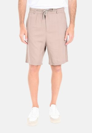 Pantaloni corti beige con vita regolabile, tasche laterali, taglio sartoriale e texture del tessuto liscia. Abbinati a sneakers bianche.