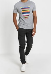 Camiseta de algodón gris con un gráfico de oso a rayas multicolores. Combinada con pantalones cargo negros y zapatillas blancas. Atuendo casual.