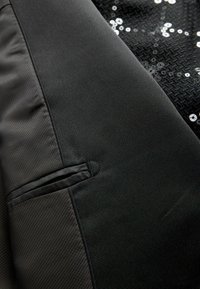 Fekete szövet, amely sima, matt részből és fényes kiegészítőkkel ellátott texturált flittermintából áll. Jobb oldalon zsebet tartalmaz.