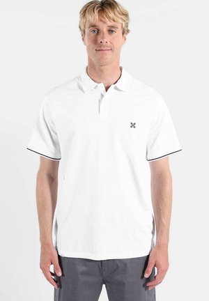 Polo blanc avec un col classique, des manches courtes, et une bordure noire sur les bords des manches. Présente un petit logo sur la poitrine gauche.