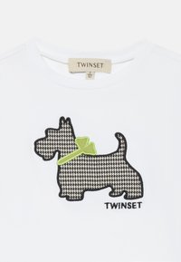 Witte katoenen t-shirt met een zwart-wit houndstooth patroon van een Scottie hond applicatie met een groene strik, gemarkeerd "TWINSET."