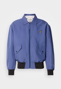 Μπλε μπουφάν τύπου bomber με φερμουάρ μπροστά, δύο λοξές τσέπες και μαύρα ριμπ μανίκια και τελείωμα. Διαθέτει κεντημένη λεπτομέρεια στέμματος στο στήθος.