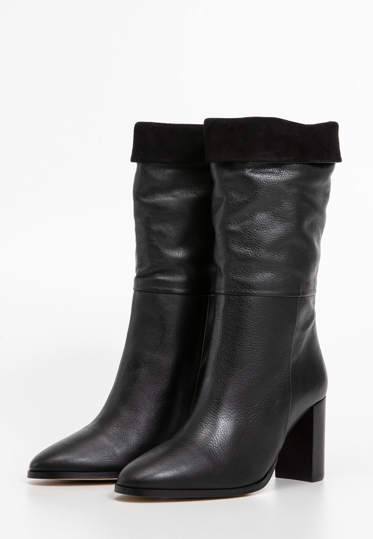 Bottines en cuir noir avec une finition lisse, un revers en daim, des bouts pointus et un talon épais. Le design est élégant et moderne.